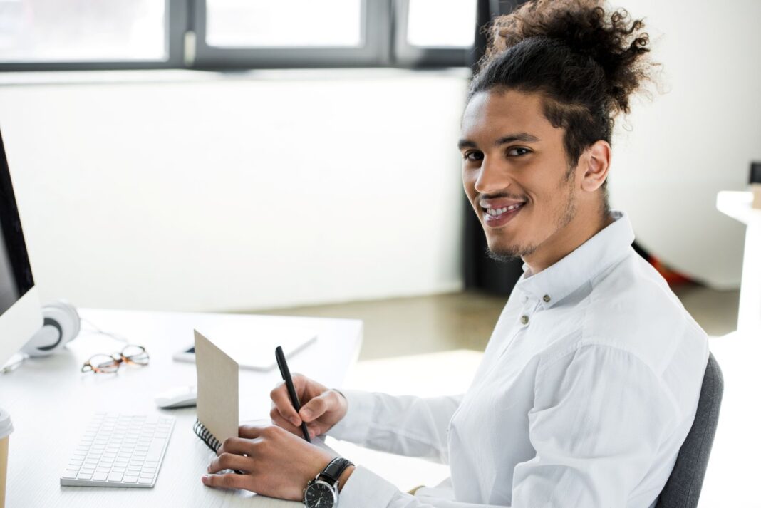 Jeune homme souriant à l'idée de rédiger sa lettre de motivation pour son apprentissage